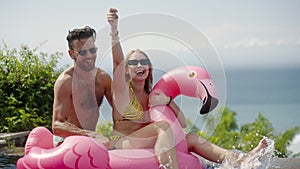 Young couple friends swim dance with inflatable pink flamingo on pool party