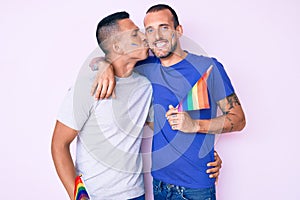 Young couple of gay men together in love holding homosexual pride colorful flag kissing with affection