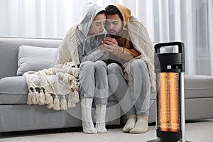 Young couple getting warm near electric heater at home