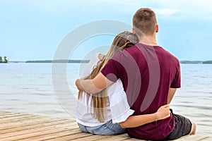 A young couple a girl and a young man sit on the beach in a Lotus position on a Wooden bridge and watch the sunset