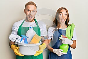 Young couple of girlfriend and boyfriend wearing apron holding products and cleaning spray celebrating crazy and amazed for