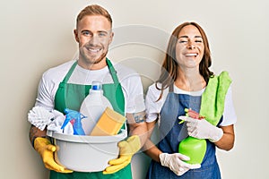 Young couple of girlfriend and boyfriend wearing apron holding products and cleaning spray smiling and laughing hard out loud