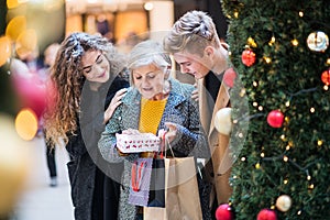 A young couple giving a present to grandmother in shopping center at Christmas.