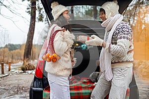 Young couple giving presents and looking each other sitting in the trunk in winter holidays.