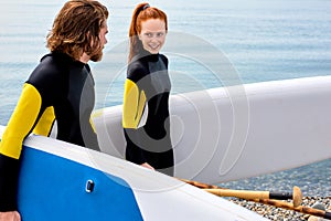 Young couple go to ocean. Redhead woman and man holding surfboard on beach