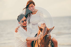 Young couple goes horse riding on tropical beach.