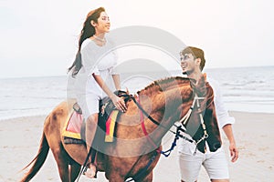 Young couple goes horse riding on tropical beach.