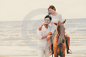 Young couple goes horse riding on tropical beach.