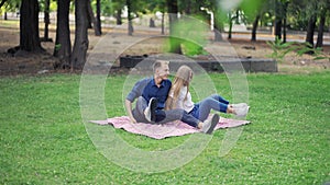 A young couple goes to the park for a picnic. The guy and the girl spread a blanket in nature and sit down to rest