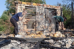 Young couple grub out of the ruins of house destroyed with fire. Damaged window, walls and floor, wooden frame.