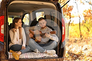 Young couple with guitar sitting in open car trunk