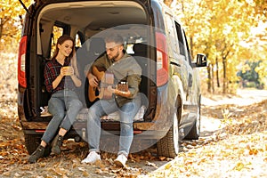 Young couple with guitar sitting in open car trunk