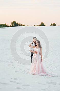 Young couple a guy in black breeches and a girl in a pink dress are walking along the white sand