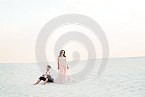 Young couple a guy in black breeches and a girl in a pink dress are walking along the white sand