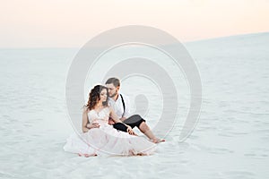 Young couple a guy in black breeches and a girl in a pink dress are walking along the white sand