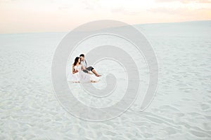 Young couple a guy in black breeches and a girl in a pink dress are walking along the white sand