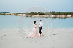 Young couple a guy in black breeches and a girl in a pink dress are walking along the white sand