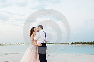 Young couple a guy in black breeches and a girl in a pink dress are walking along the white sand