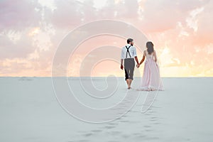 Young couple a guy in black breeches and a girl in a pink dress are walking along the white sand