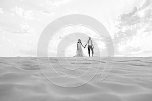 Young couple a guy in black breeches and a girl in a pink dress are walking along the white sand