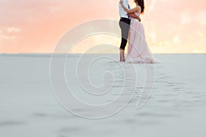 Young couple a guy in black breeches and a girl in a pink dress are walking along the white sand