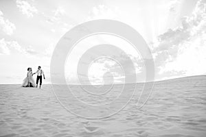 Young couple a guy in black breeches and a girl in a pink dress are walking along the white sand