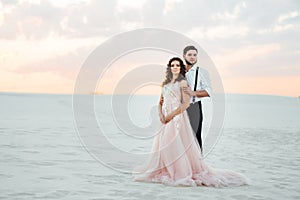 Young couple a guy in black breeches and a girl in a pink dress are walking along the white sand