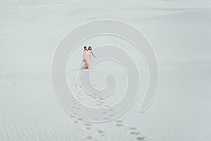 Young couple a guy in black breeches and a girl in a pink dress are walking along the white sand