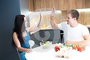 Young couple handsome husband and his beautiful wife cooking breakfast in the kitchen together giving high five looking