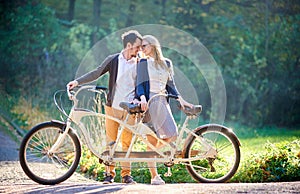 Young couple, handsome man and attractive woman on tandem bike in sunny summer park or forest.