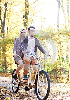 Young couple, handsome man and attractive woman on tandem bike in sunny summer park or forest.