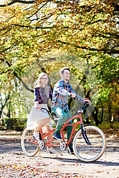 Young couple, handsome man and attractive woman on tandem bike in sunny summer park or forest.