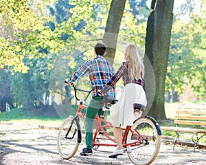 Young couple, handsome man and attractive woman on tandem bike in sunny summer park or forest.