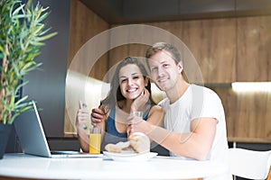 Young couple handsome man and beautiful woman looks happy working in laptop while having croissants with orange juice