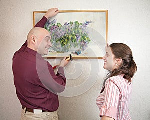 Young couple hanging art picture on wall at