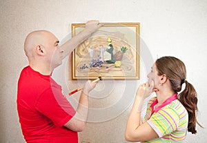 Young couple hanging art picture on wall at