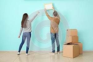 Young couple hanging picture on wall in their new house