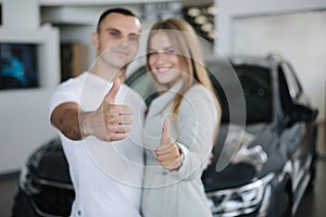 Young couple happy after buying new car from car showroom. Man and woman give thumb up. Focus on hands