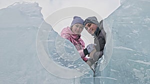 Young couple has fun during winter walk against background of ice of frozen lake. Love story. Lovers hide behind the ice