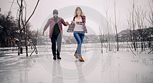 Young couple has fun during winter walk on ice of frozen lake.
