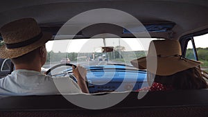 Young couple in hats riding at vintage car during road trip. Unrecognizable man and woman sitting at the front seat of