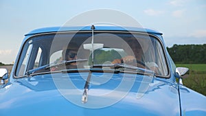 Young couple in hats riding at vintage car during summer travel. Happy man and woman sitting at the front seat of old