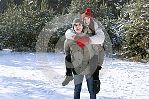 Young couple have a fun in winter forest. Guy rolls the girl on his back