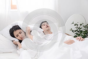 Young couple have problem with man`s snoring. Heterosexual couple in bed, man sleeps and snoring with mouth open, while a tired