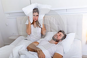 Young couple have problem with man`s snoring. Heterosexual couple in bed, man sleeps and snoring with mouth open, while a tired