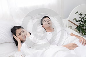 Young couple have problem with man`s snoring. Heterosexual couple in bed, man sleeps and snoring with mouth open, while a tired