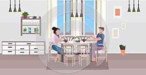 Young couple having breakfast man woman sitting at table eating food together modern home kitchen interior flat