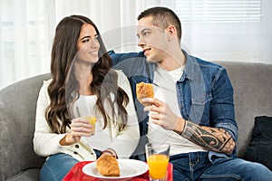 Young couple having breakfast together while sitting on couch at home.