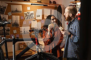 Young couple having a cheerful conversation and eating delicious hamburgers while standing in a bicycle repair shop