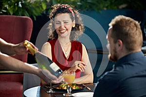 Young couple having dinner in restaurant. Waiter brought a bottle of champagne